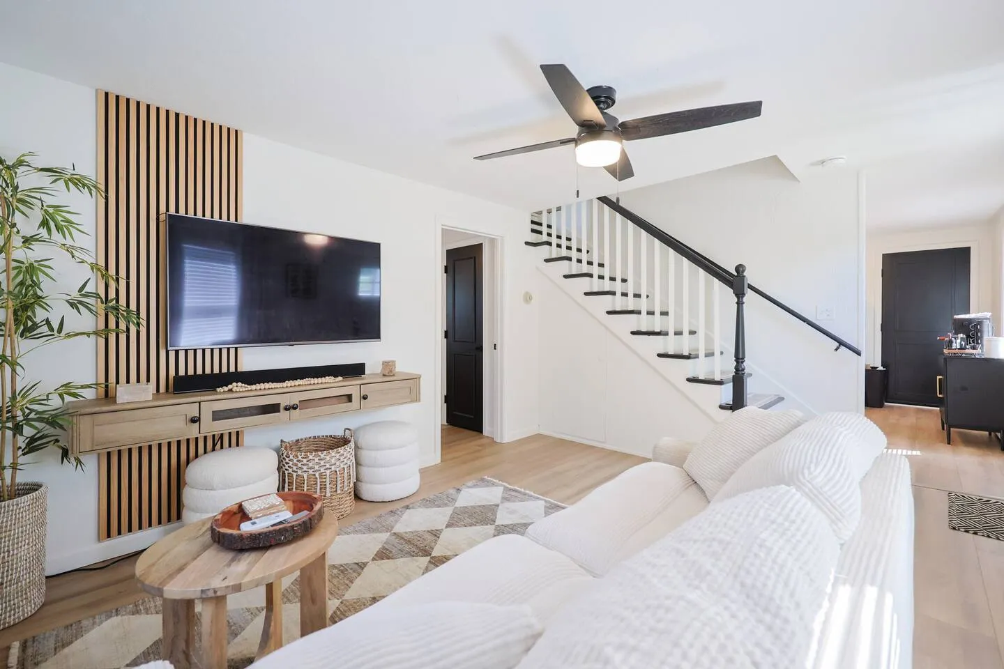 The living room of the flagship home: a cream sofa, a wood slat wall with a mounted television and a black-railed staircase.
