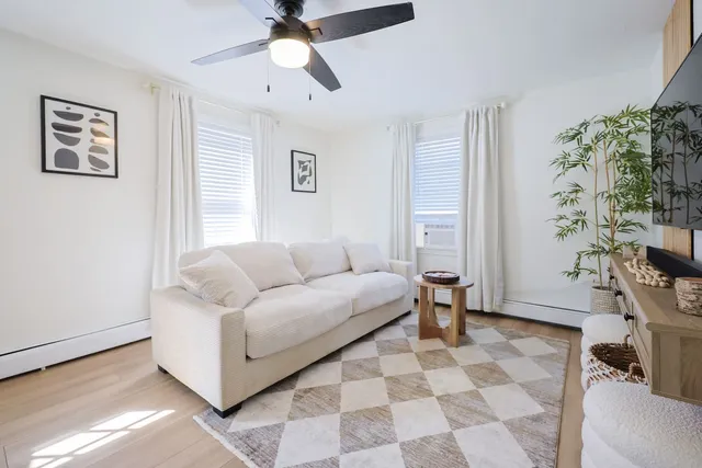 The living room of the flagship home: a cream sofa, a checkered rug and a plant by the window.