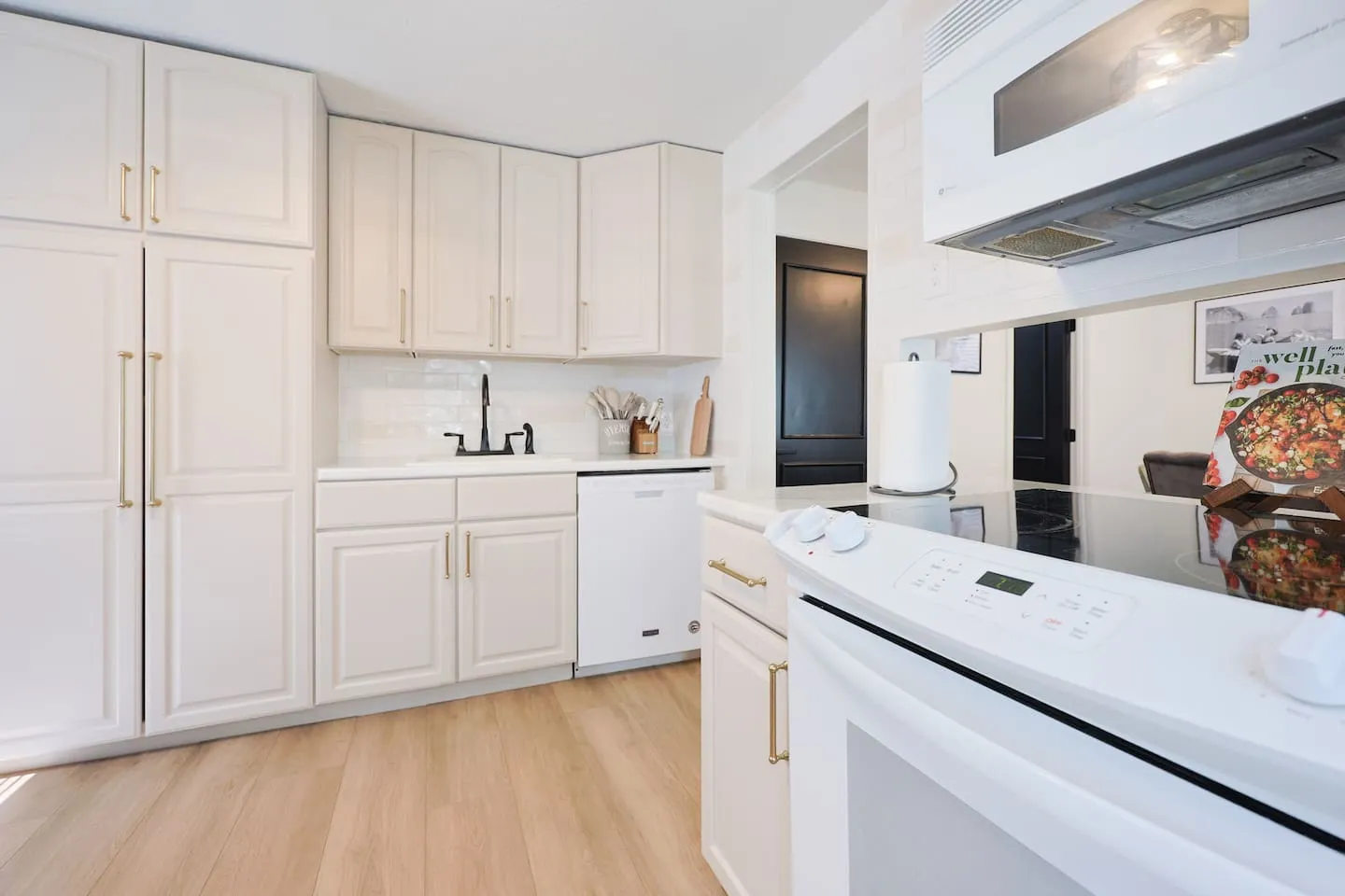 The kitchen: white cabinets with gold handles, a white range and dishwasher, and light wood floors.